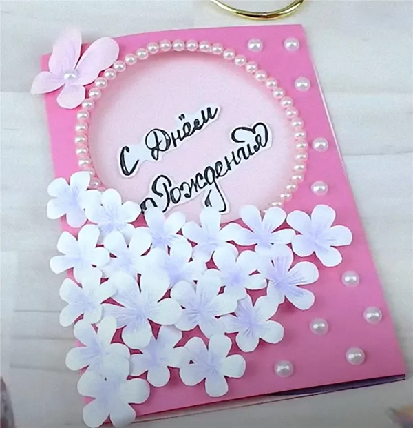 Открытка с днем рождения сделана из розовой бумаги, украшена белыми цветами из бумаги, полубусинами