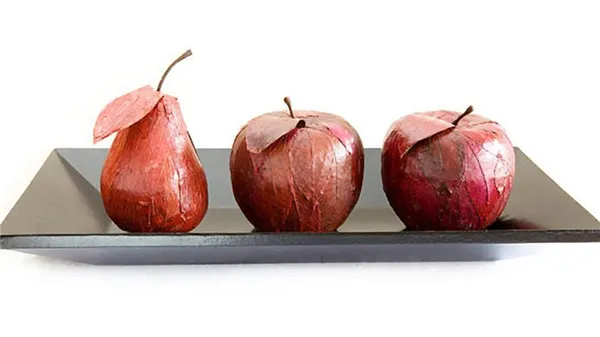 На тарелке лежит груша и два яблока из папье-маше. Муляжи окрашены в бордовый цвет