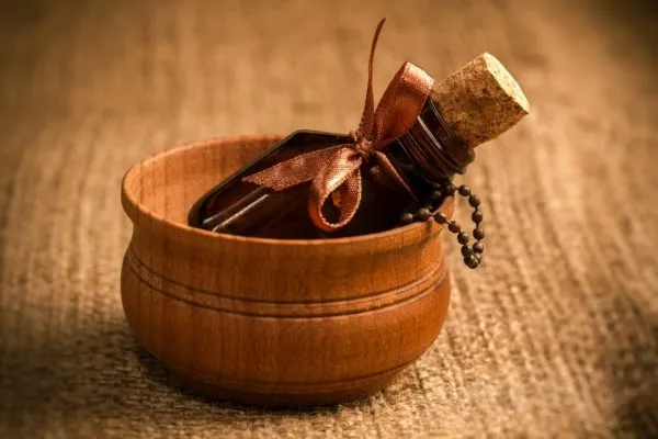 Бутылочка из тёмного стекла, перевязанная коричневой декоративной лентой, лежит в деревянной круглой коробочке